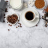 دانه‌های تازه قهوه کنار آسیاب دستی و ابزار دم‌آوری خانگی روی میز چوبی